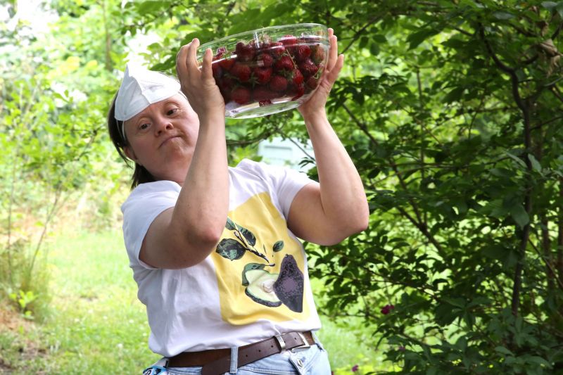 Die Bewohnerin unserer LebensOrte trägt eine Schüssel voller frisch gepflückter Erdbeeren durch den Garten beim Sommerfest