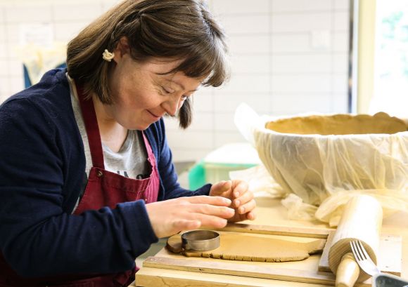 Eine Keramikerin aus unserer Keramikwerkstatt sticht mit Formen aus und lächelt dabei